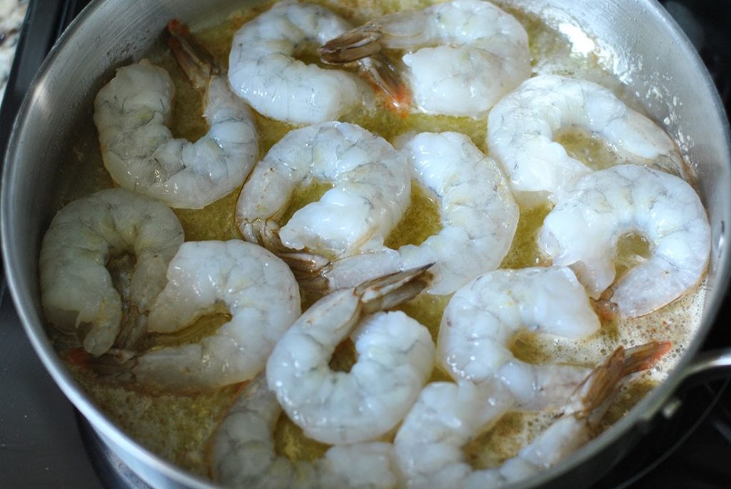 Shrimp being sautéed. The uncooked side is white and facing upwards