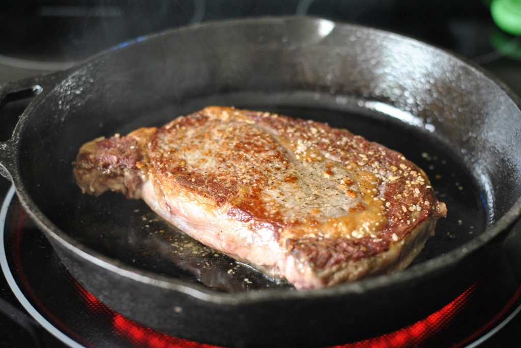 Searing steak in skillet, one side already seared and flipped