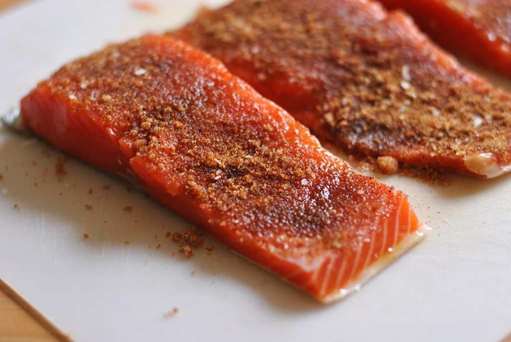 Four raw salmon fillets with spices on, ready to grill
